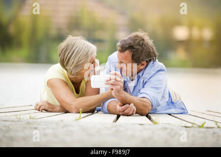 Coppia senior sdraiato e tenendo selfie sul molo Foto Stock