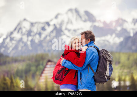 Senior escursionisti giovane kissing durante la passeggiata nelle splendide montagne, colline e hotel in background Foto Stock