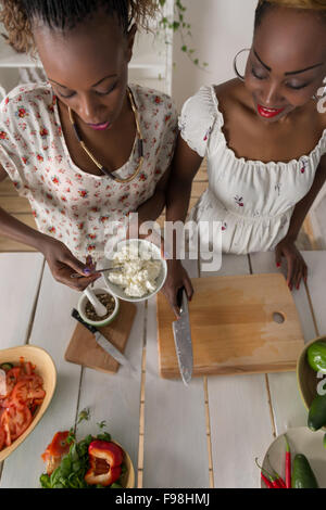 Due donne africane per la cottura in cucina rendendo il cibo sano con insalata di verdure. Vista superiore Foto Stock