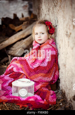 Outdoor ritratto di incantevole piccola ragazza seduta e avvolto nella coperta Foto Stock