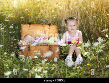 Estate outdoor ritratto di incantevole piccola ragazza seduta sul prato con sua sorella bambino giacente nella vecchia valigia Foto Stock