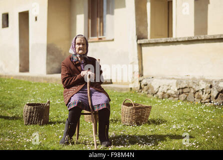 Molto vecchia donna con testa sciarpa sedersi e rilassarsi in giardino Foto Stock