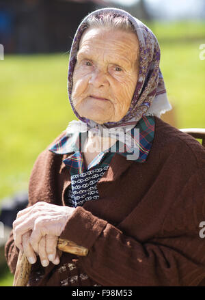 Molto vecchia donna con testa sciarpa sedersi e rilassarsi in giardino Foto Stock