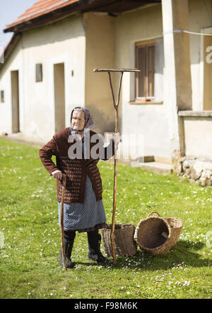 Molto vecchia donna in testa sciarpa con attrezzi da giardino nella sua iarda posteriore Foto Stock