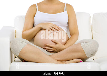 Ritratto in studio di un irriconoscibile incinta Donna seduta sul divano isolati su sfondo bianco Foto Stock