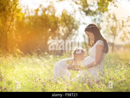 Carino bambina abbracciando e baciando la madre incinta pancia in estate la natura Foto Stock