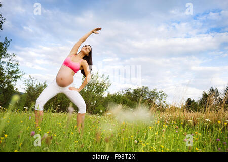 Felice giovane donna incinta che esercitano in estate la natura Foto Stock