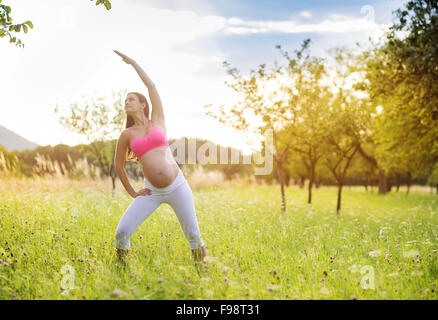 Felice giovane donna incinta che esercitano in estate la natura Foto Stock