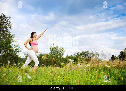 Felice giovane donna incinta che esercitano in estate la natura Foto Stock