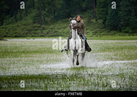 Una ragazza cavalca un cavallo bianco in acqua a Capilla vieja, Estado de Mexico, Messico. (Sfocatura) Foto Stock