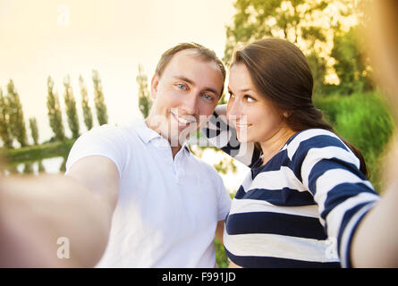 Felice giovane incinta giovane costeggiata in natura e prendendo selfie Foto Stock