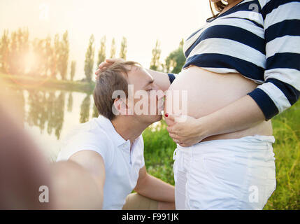 Felice giovane incinta giovane costeggiata in natura e prendendo selfie Foto Stock