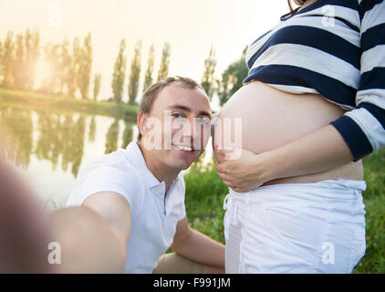 Felice giovane incinta giovane costeggiata in natura e prendendo selfie Foto Stock