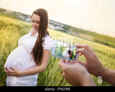 Uomo di scattare una foto con lo smartphone di bella donna incinta nel campo Foto Stock