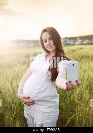 Felice giovane donna incinta prendendo selfie nel campo Foto Stock