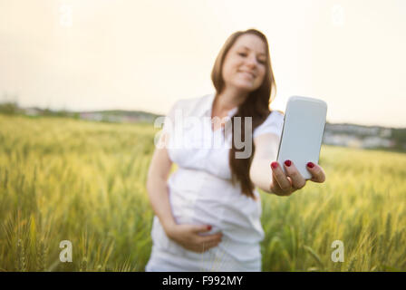 Felice giovane donna incinta prendendo selfie nel campo Foto Stock