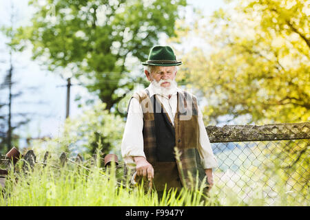 Vecchio contadino con la barba e il cappello è camminare nella sua iarda posteriore Foto Stock