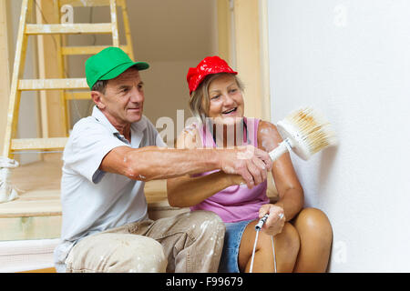 Active senior giovane pittura parete con la spazzola nella nuova casa. Si stanno divertendo. Foto Stock