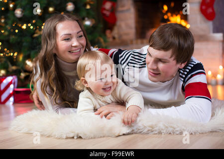 Felice giovani genitori e figli hanno un divertimento vicino a albero di Natale a casa. Padre, madre e figlio per celebrare il nuovo anno insieme