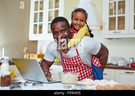 Giovane uomo alla ricerca di ricetta in rete con la figlia sulla sua schiena Foto Stock