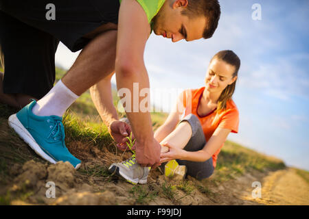 Pregiudizio - sport donna con twisted storte Come ottenere aiuto da uomo di toccare la sua caviglia. Foto Stock