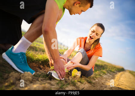 Pregiudizio - sport donna con twisted storte Come ottenere aiuto da uomo di toccare la sua caviglia. Foto Stock