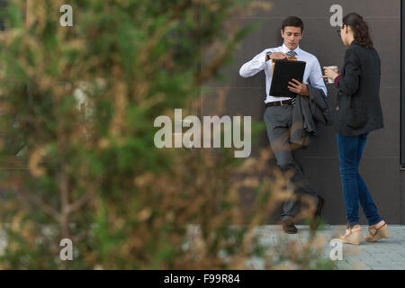 Due colleghi in piedi all'aperto vicino edificio per uffici e parlare Foto Stock