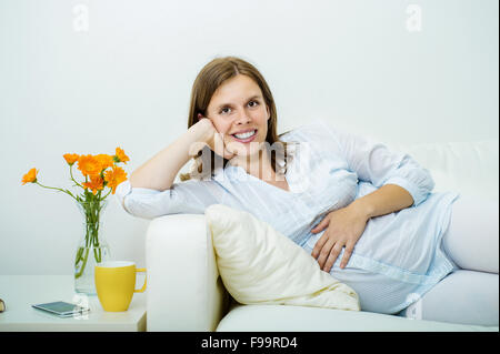 Ritratto in studio di stanchezza donna incinta sdraiato sul divano isolati su sfondo bianco Foto Stock