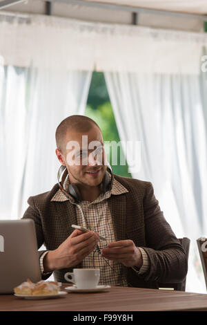 Business man in appoggio al cafe e ascolto di musica con cuffie vintage Foto Stock