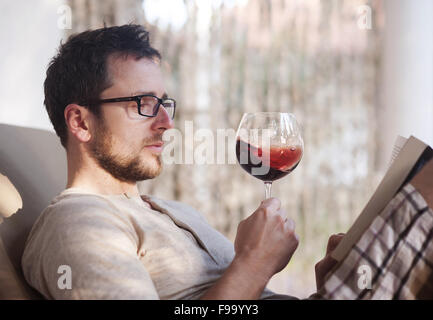 Giovane uomo bello rilassarsi, leggere libri e bere vino rosso Foto Stock