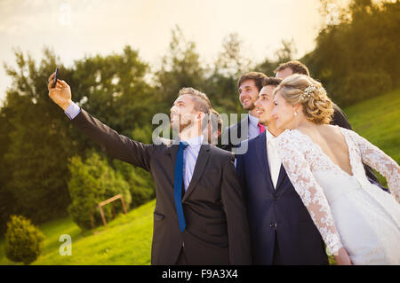 Outdoor Ritratto di giovane e bella sposa con lo sposo e i suoi amici prendendo selfie Foto Stock