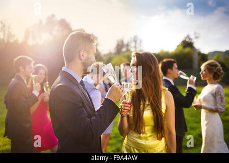 Gli ospiti dei matrimoni bicchieri tintinnanti mentre agli sposi novelli bevendo champagne in background Foto Stock