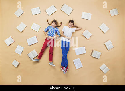 Dei bambini felici sdraiati sul pavimento con un gruppo di libri Foto Stock