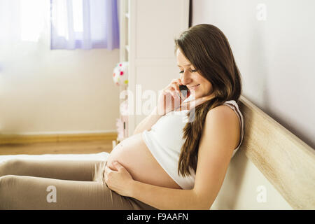 Bella donna incinta parlando al telefono mobile nella sua camera da letto Foto Stock