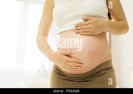 Bella donna incinta applicando anti smagliature o crema idratante Foto Stock