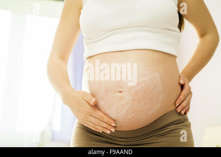 Bella donna incinta applicando anti smagliature o crema idratante Foto Stock