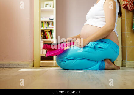 Ritratto di un irriconoscibile donna incinta tenendo la paletta e ginestra, pulizia casa Foto Stock