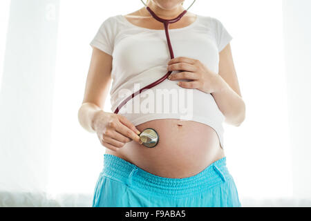 Close-up di un irriconoscibile donna incinta con sthetoscope e le mani sulla pancia Foto Stock