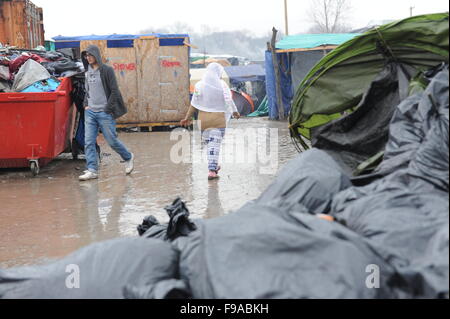 Fila di docce temporanee sporche e servizi igienici nel campo profughi della giungla in rifugiati corrono attraverso la pioggia nella giungla, Calais in una mattinata invernale. Le docce corrono solo su acque fredde e i servizi igienici sono sporchi perché non vengono puliti abbastanza spesso. In primo piano sono traboccanti cassonetti di rifiuti forniti dal governo francese. Foto Stock