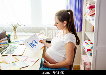 Donna incinta in ufficio a casa con il computer portatile Foto Stock