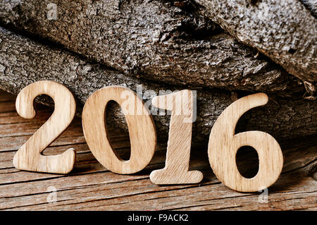 Numeri in legno formando il numero 2016, come il nuovo anno con un mucchio di tronchi in background su un rustico di una superficie di legno Foto Stock