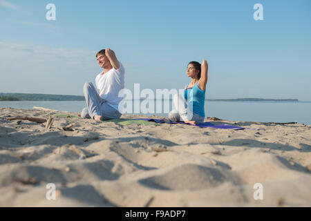 Coppia giovane facendo stretching esercizi yoga con il mare sullo sfondo Foto Stock