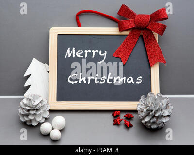 'Buon Natale' scritta sulla lavagna con un nastro rosso e pigne Foto Stock
