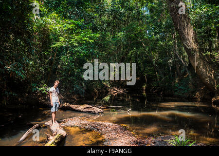 Giovane uomo in piedi sul log in fiume nella giungla, Kuala Tahan, Taman Negara, Malaysia Foto Stock