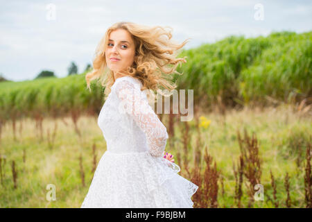 Sposa felice: un giovane biondo dai capelli donna che indossa un lacy bianco abito da sposa all'aperto in un campo in un pomeriggio autunnale, Foto Stock