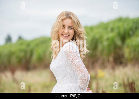 Sposa felice: un giovane biondo dai capelli donna che indossa un lacy bianco abito da sposa all'aperto in un campo in un pomeriggio autunnale, Foto Stock