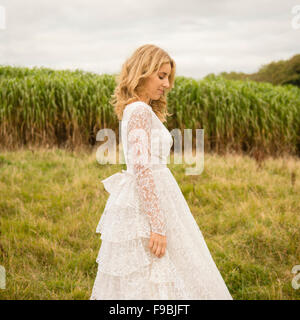 Un profilo laterale di una giovane dai capelli biondi donna che indossa un lacy bianco abito da sposa all'aperto in un campo in un pomeriggio autunnale, Foto Stock