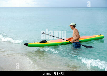 A sessant anni di vecchio uomo caucasico guida la sua paddleboard gonfiabile in spiaggia off St. Croix, U.S. Isole Vergini. Foto Stock