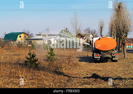 La spruzzatura di acqua su alberi giovani nel parco da strada carrello degli sprinkler. Foto Stock