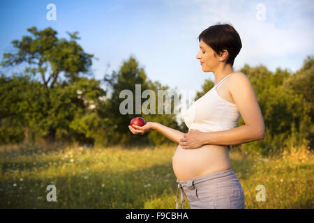 Ritratto di giovane donna incinta mangiare apple nella natura Foto Stock